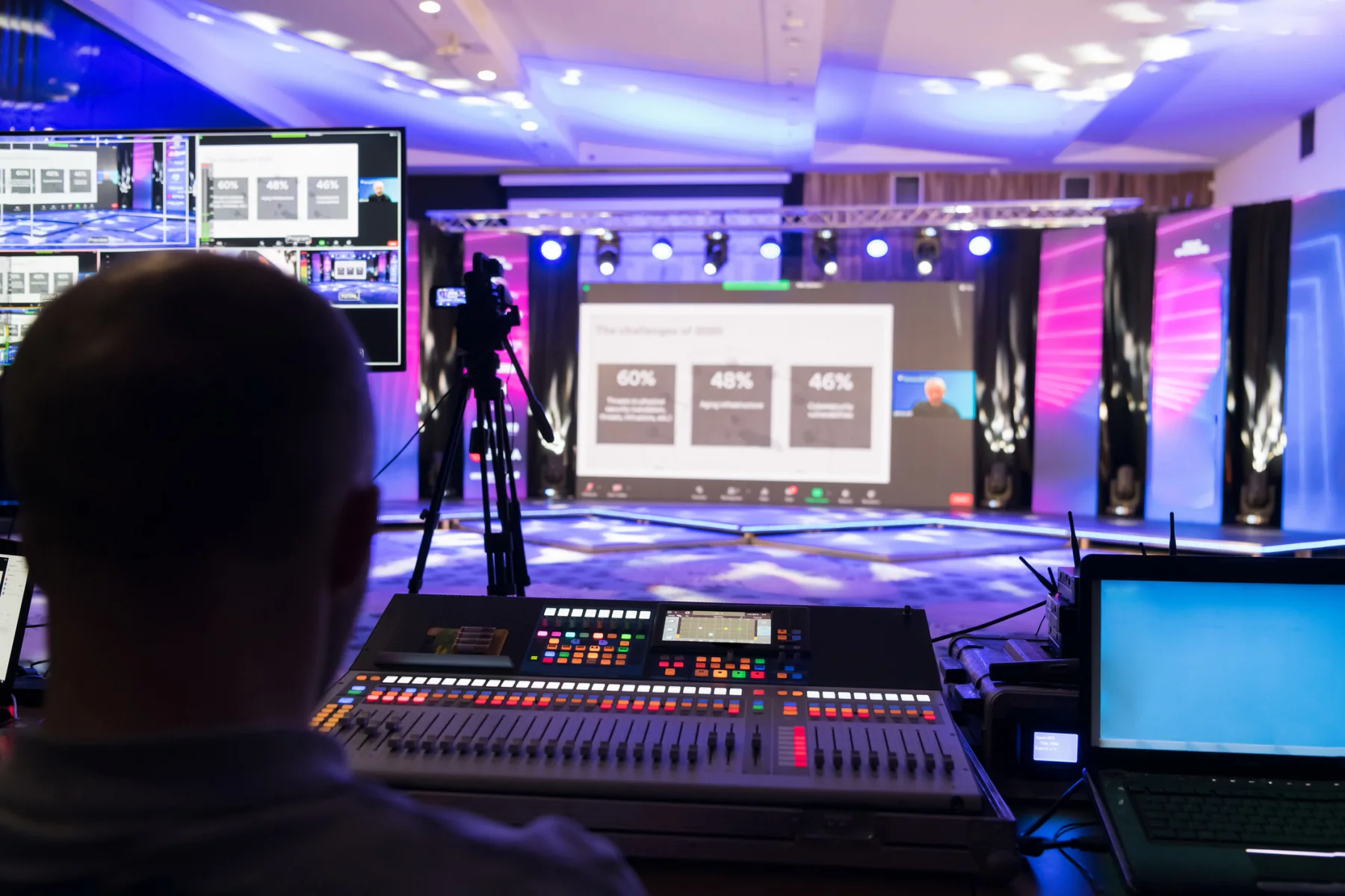 Large-scale broadcast event with staging, production infrastructure, support workstations, and event staff coordinating a live media setup