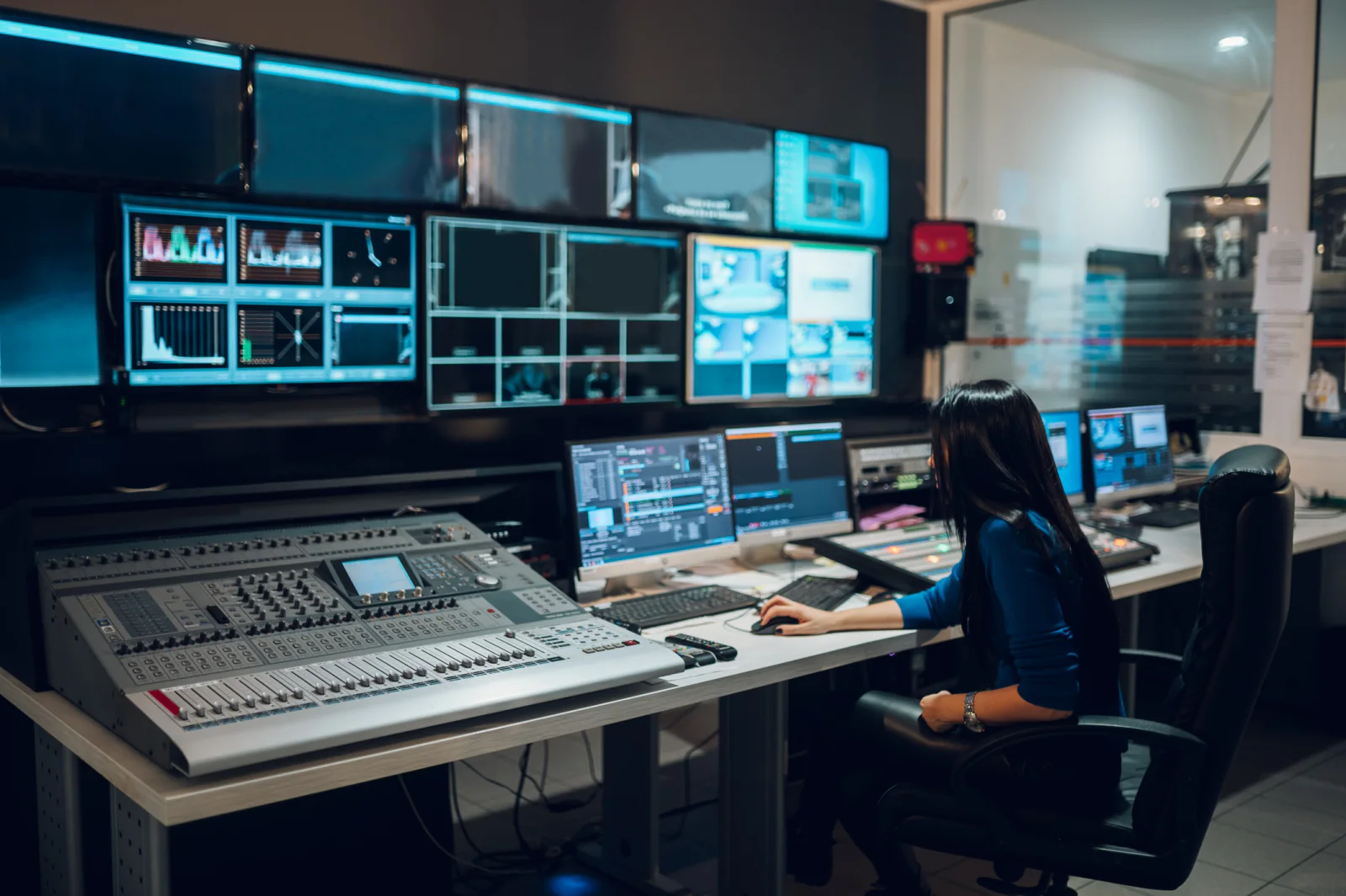 Broadcast control room with operators, production workstations, and multiple live video monitors