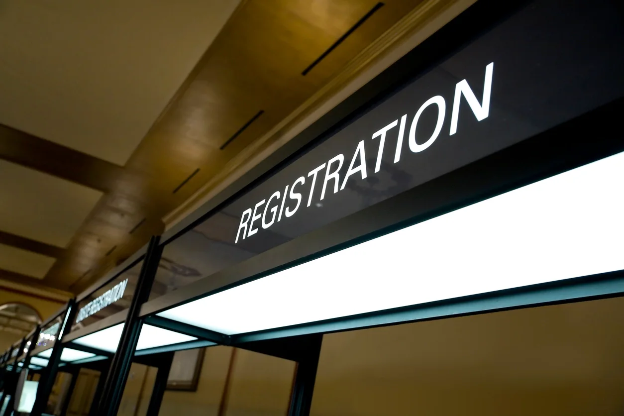 Convention center registration area with check-in tablets, badge printers, staffed counters, and attendees lining up