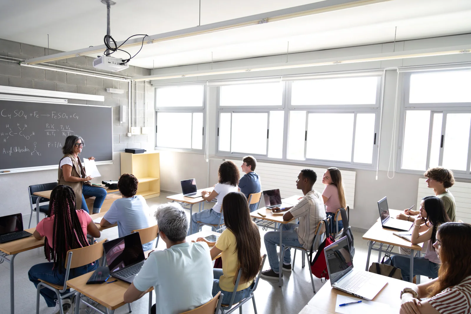 K-12 classroom with rows of student laptops and Chromebooks, charging carts, and teachers supporting a temporary 1 to 1 device rollout