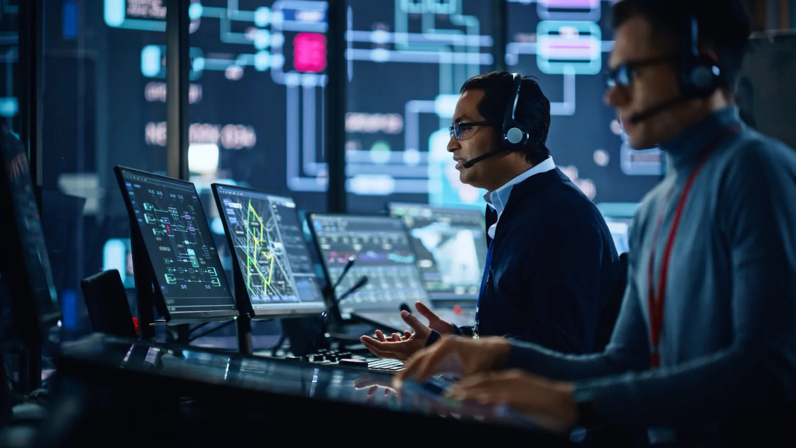 Energy monitoring room with operators reviewing dashboards on dual monitors and large status displays during active operations