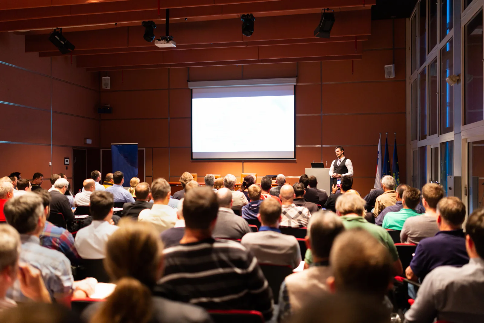 Hotel conference with attendees seated in a ballroom watching a presentation on large screens