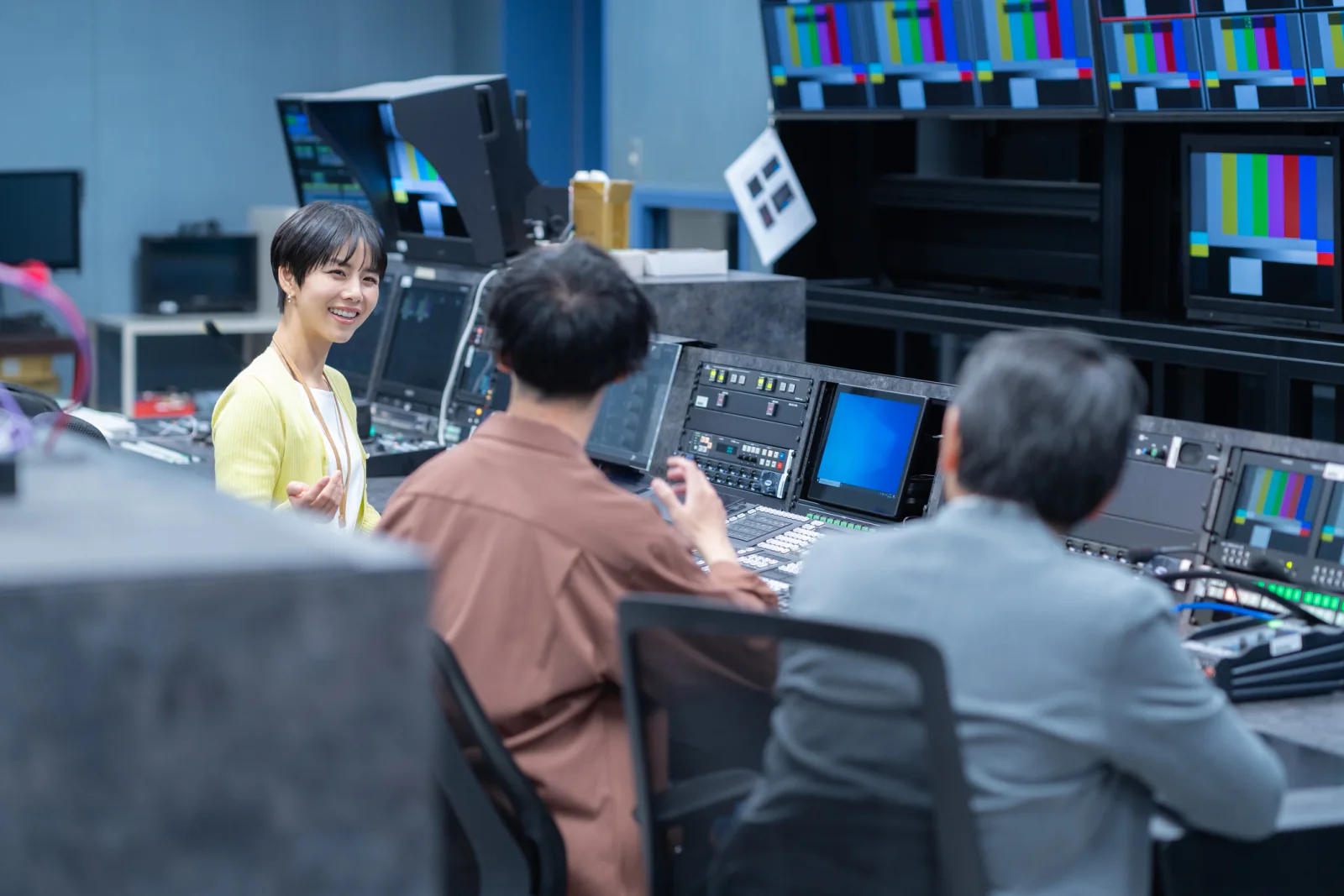Modern newsroom or studio operations room with editors and producers working at dual-monitor stations and large broadcast displays