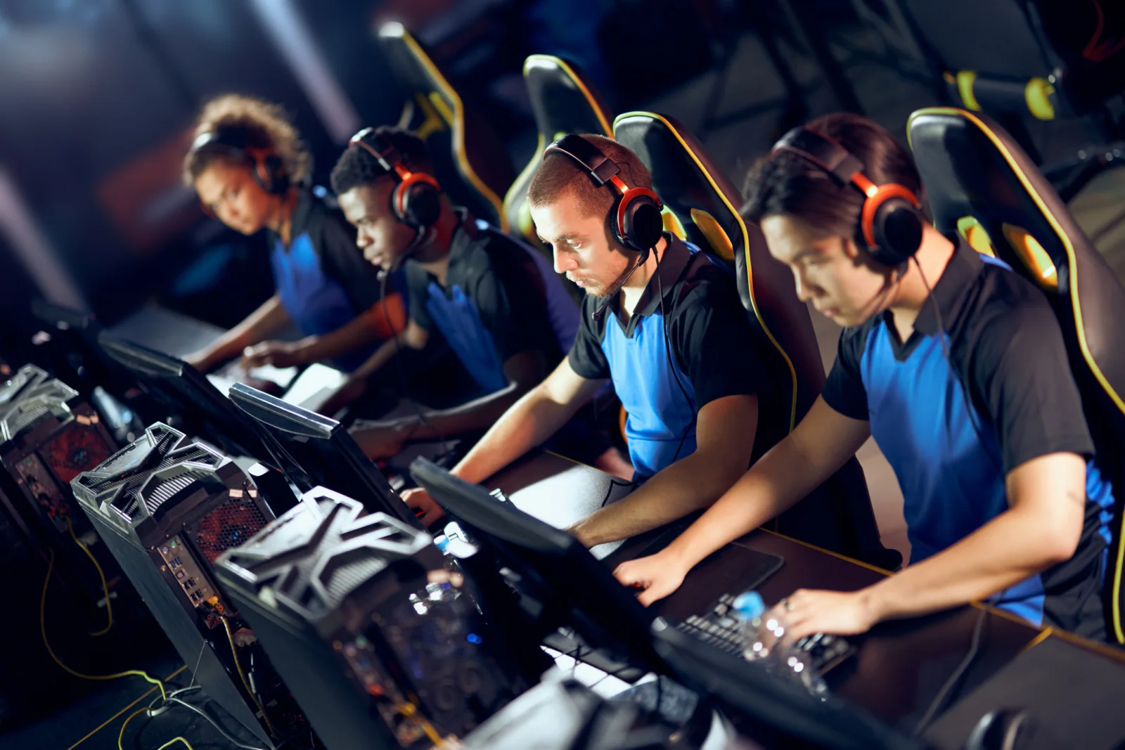 Esports tournament floor with rows of gaming PCs, low-latency monitors, players wearing headsets, and organized competitive stations