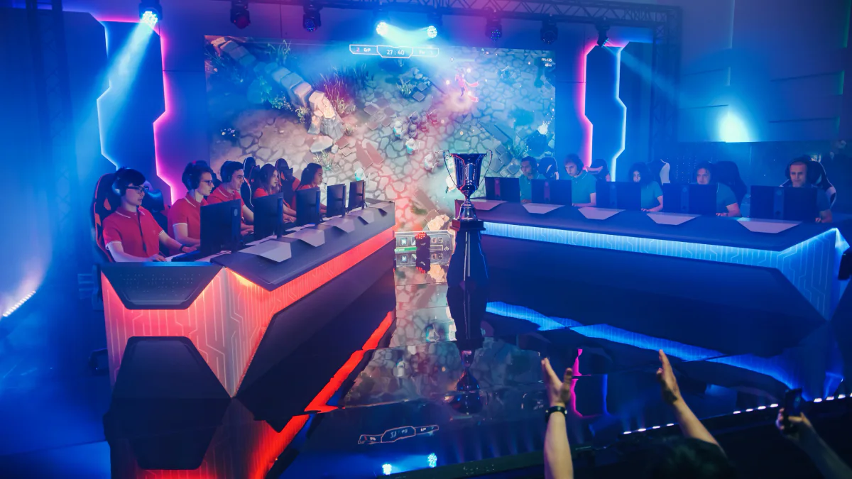 Esports finals stage with players at gaming stations, large LED displays, caster desk, and audience-facing competition setup