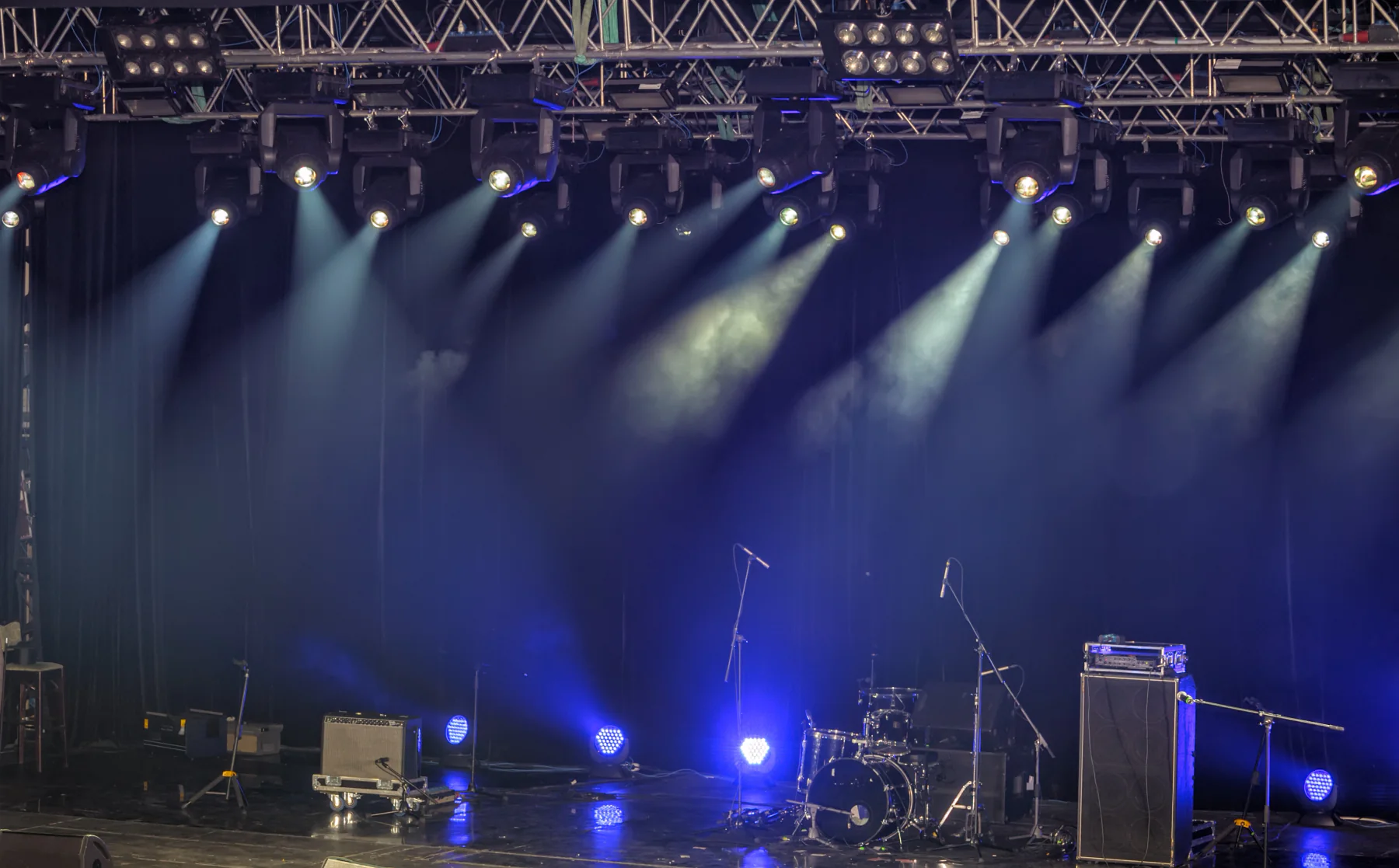 Concert backstage operations area with production staff using laptops, tablets, and support equipment during a live music event