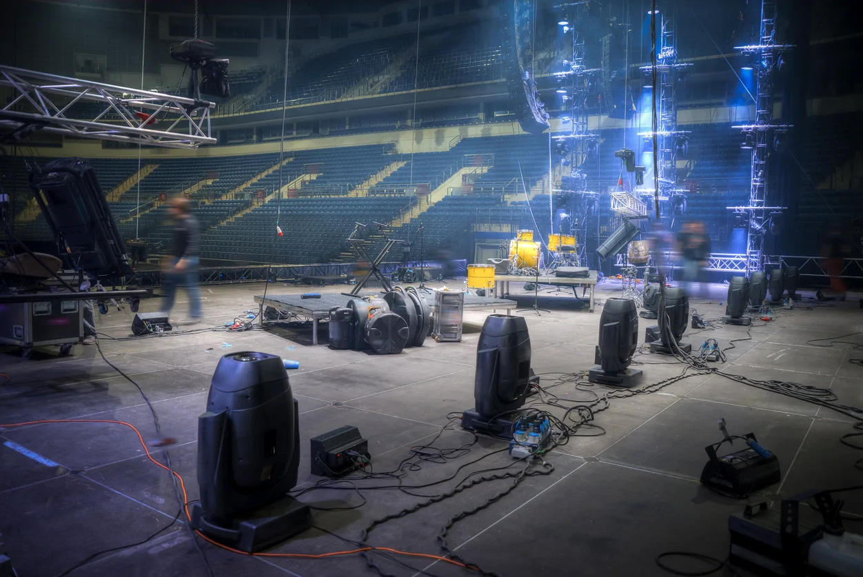 Backstage concert operations area with producers and coordinators using laptops, tablets, and support equipment during a live show