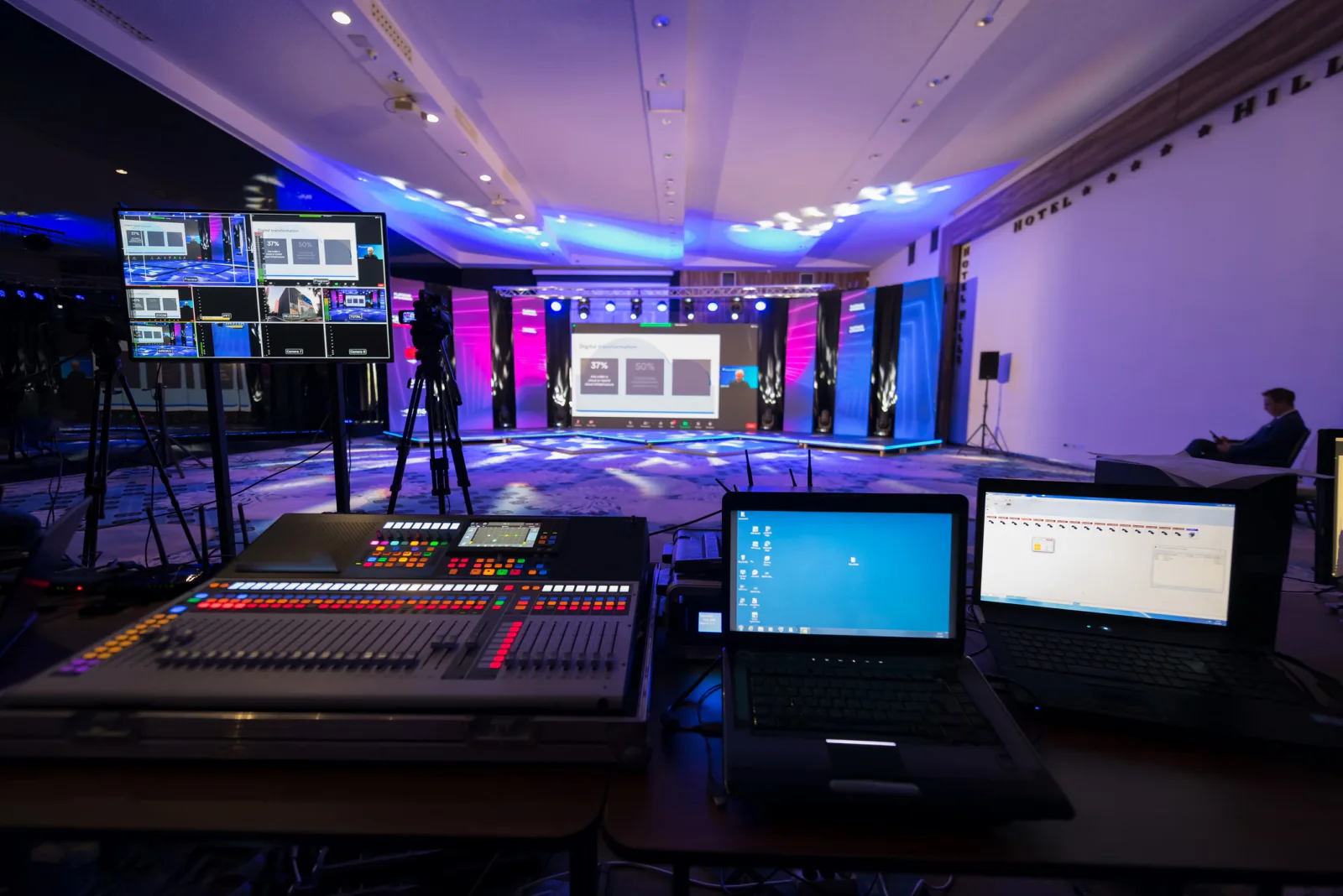 Large conference venue with multiple breakout rooms and event production staff coordinating laptops, displays, and room technology