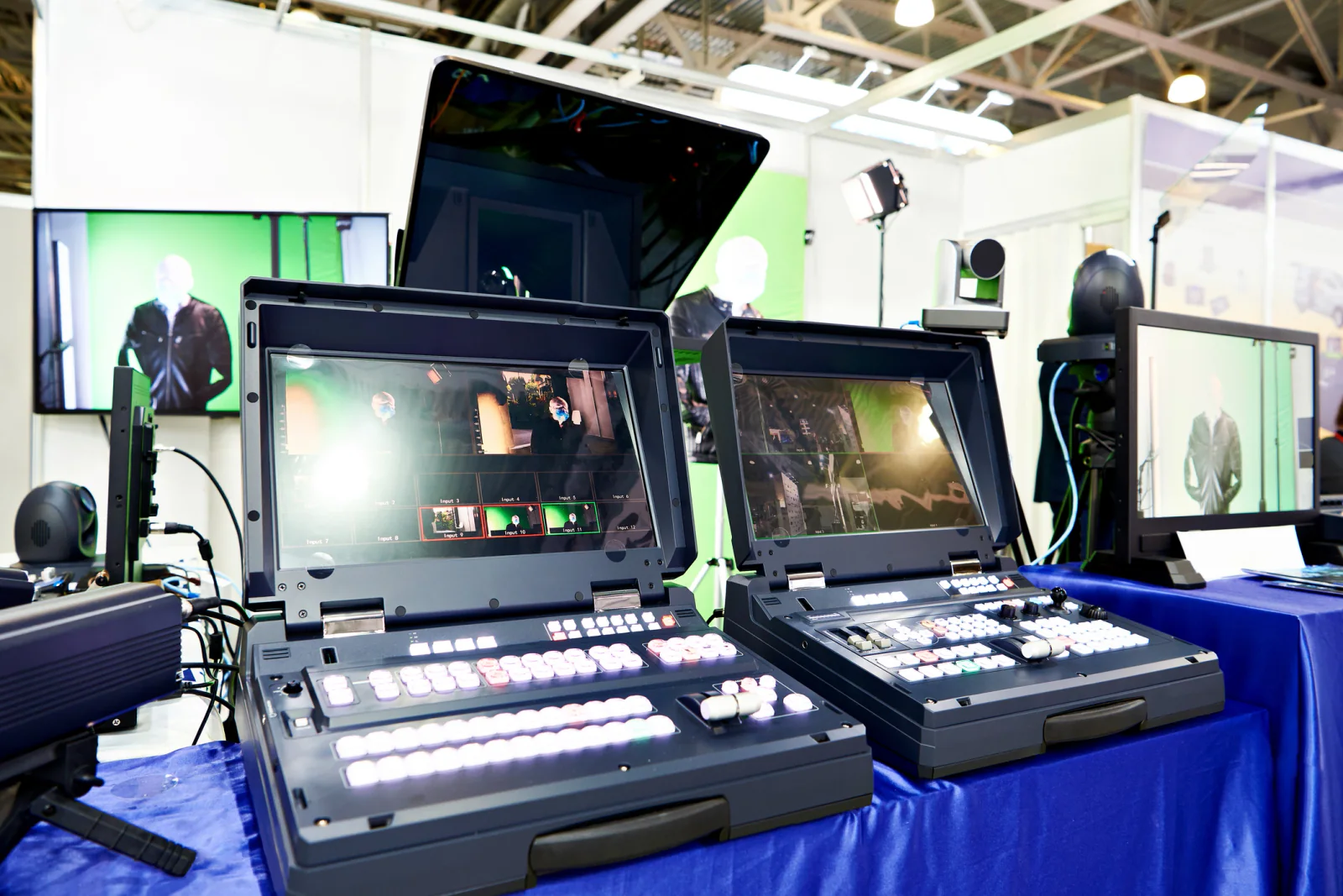 Event presenter support area with laptops, presentation screens, adapters, and technical staff preparing a live session