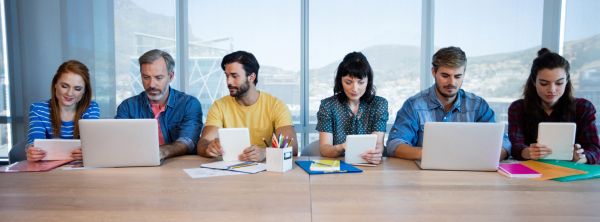 Several people at a conference table using tablets or laptops