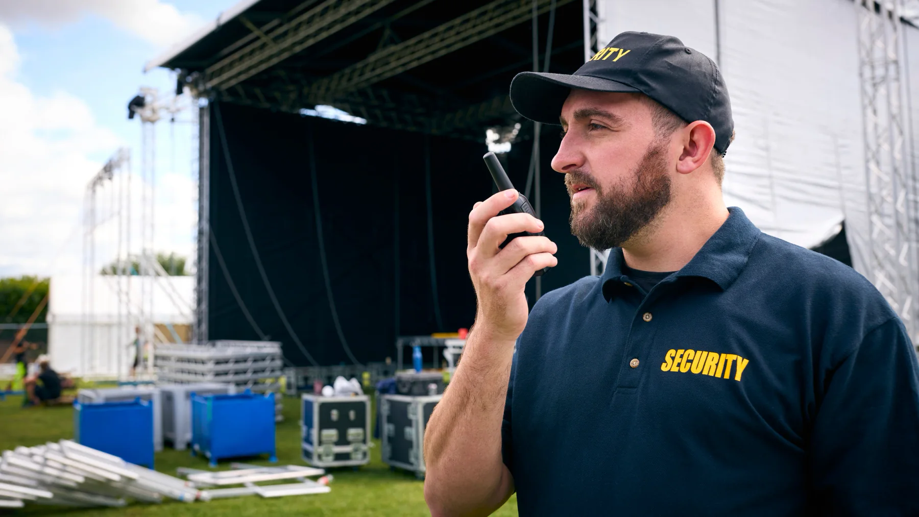 Event security staff member using a handheld two-way radio near a live event stage
